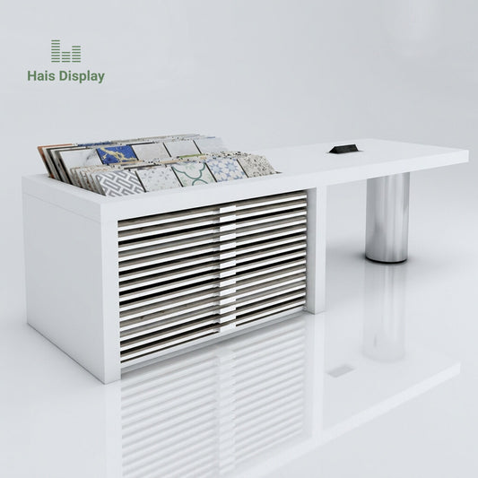 Modern white tile showroom consultation desk with embedded top tile display rack, horizontal sample storage slots, and stainless steel support leg